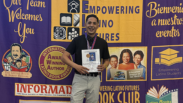 Dr. Felipe Mercado, assistant professor of social work, holding a Gold Medal for Best Reference Book in front of the the 2026 International Latino Book Awards banner.