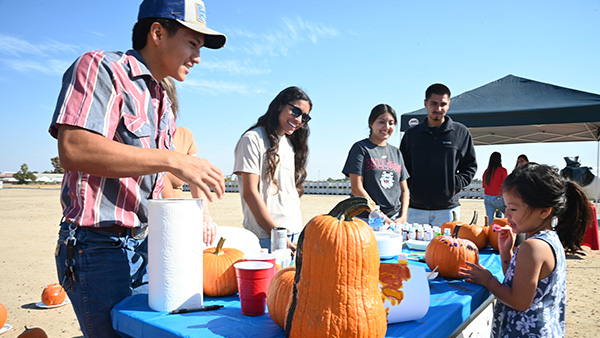 A group of people standing at a table watching a child paint a pumpkin.